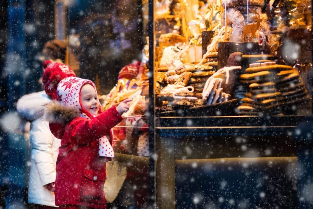 Children window shopping on traditional Christmas market in Munich, Germany on snowy winter day. 