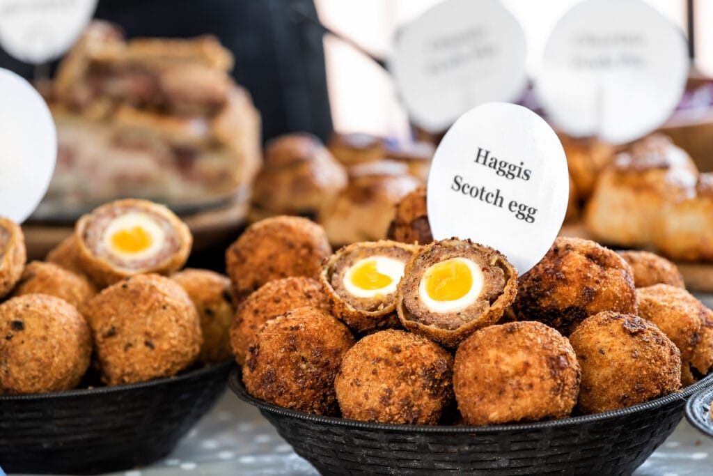 Closeup bowl of Haggis Scotch deep fried eggs with sign in market street food fair, cross section cut open, yellow yolk, breading tradition.